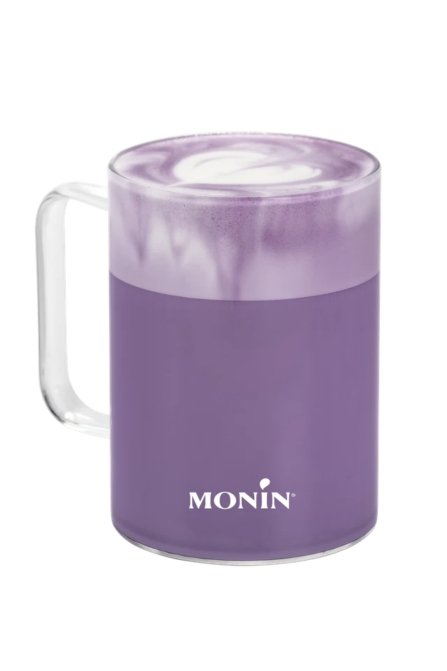 Horké fialové Ube latte MONIN ve skleněném hrnku na průhledném pozadí.