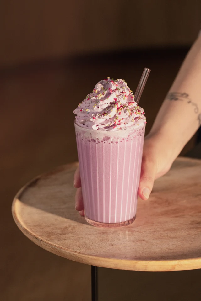 Ube frappé se šlehačkou servírované na dřevěném stolku.
