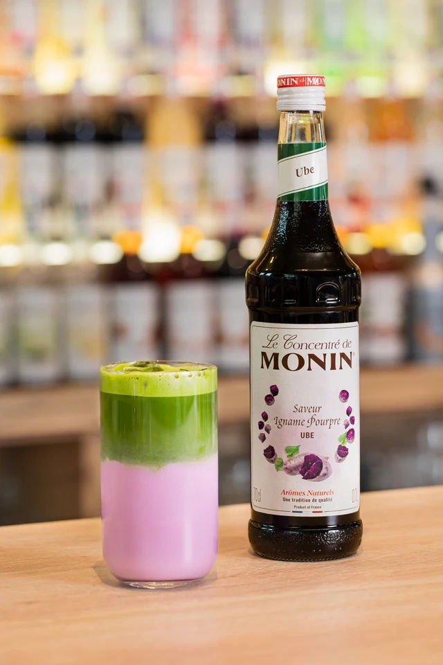 Horké Ube matcha latte vedle lahve MONIN Ube na baru.