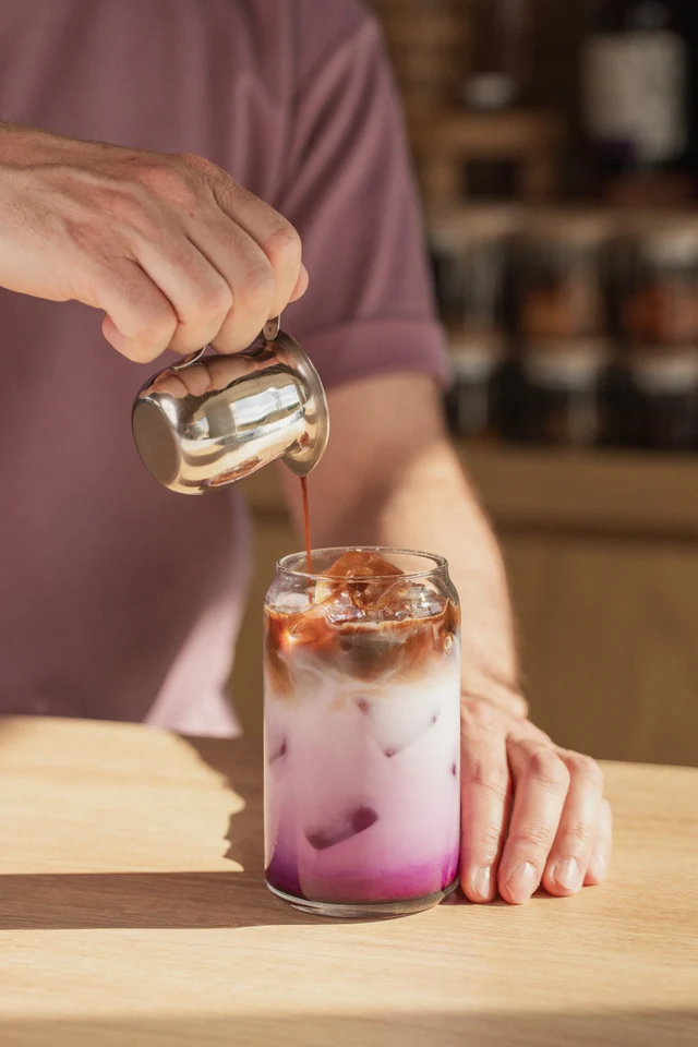 Barista přelévá espresso do vrstveného ledového Ube latte.