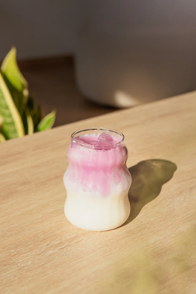 Růžovofialové ledové Ube latte ve zvlněné sklenici na dřevěném stole.