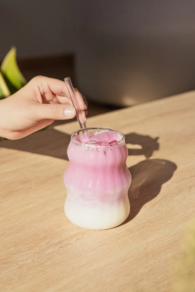 Ruka míchá růžovofialové ledové Ube latte na dřevěném stole.