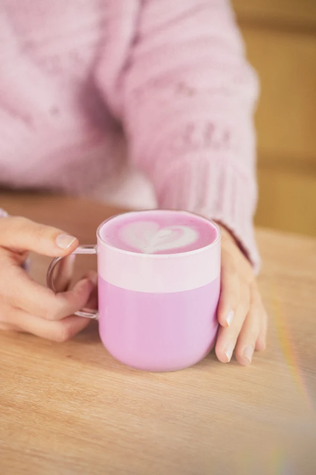 Horké růžovofialové Ube latte držené u dřevěného stolu.