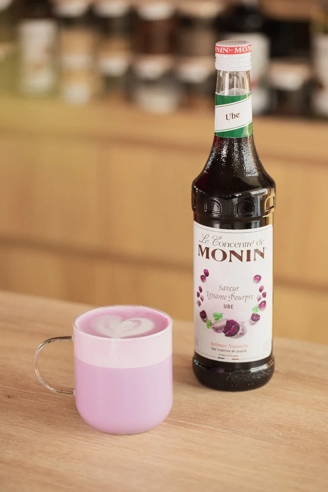 Horké Ube latte vedle lahve MONIN Ube v kavárně.