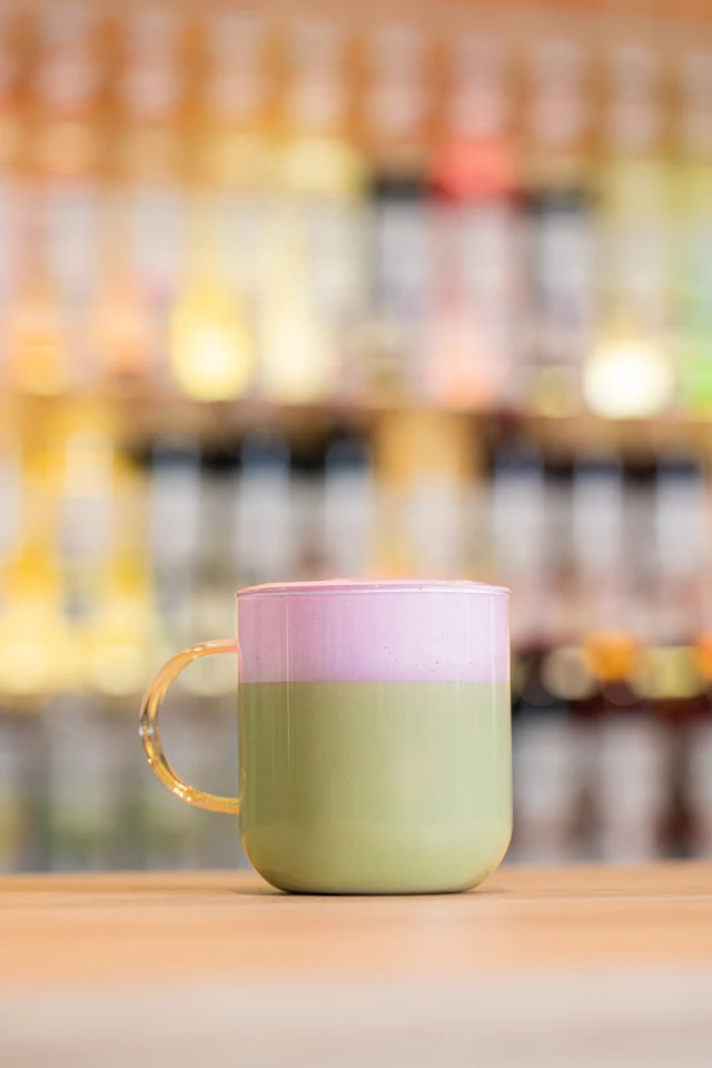 Horké zelené matcha latte s růžovofialovou Ube pěnou na baru.