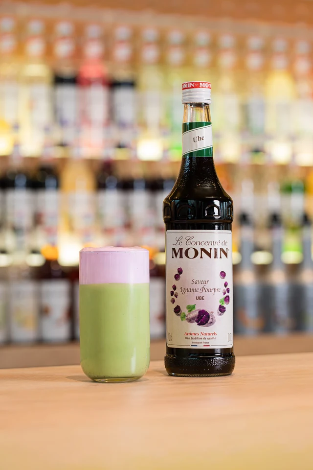 Zelenofialové Ube matcha latte vedle lahve MONIN Ube na baru.